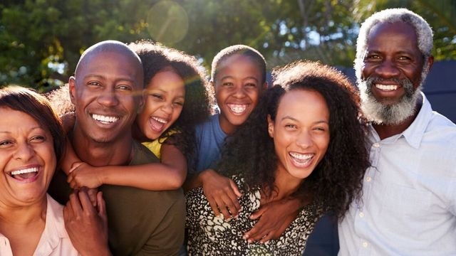 Three generations of one family crowded together outdoors, laughing in bright sunlight